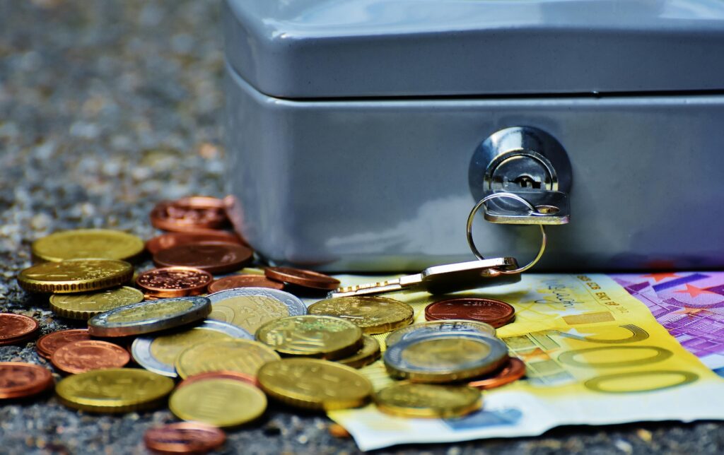 banknotes and coins besides a grey safety box