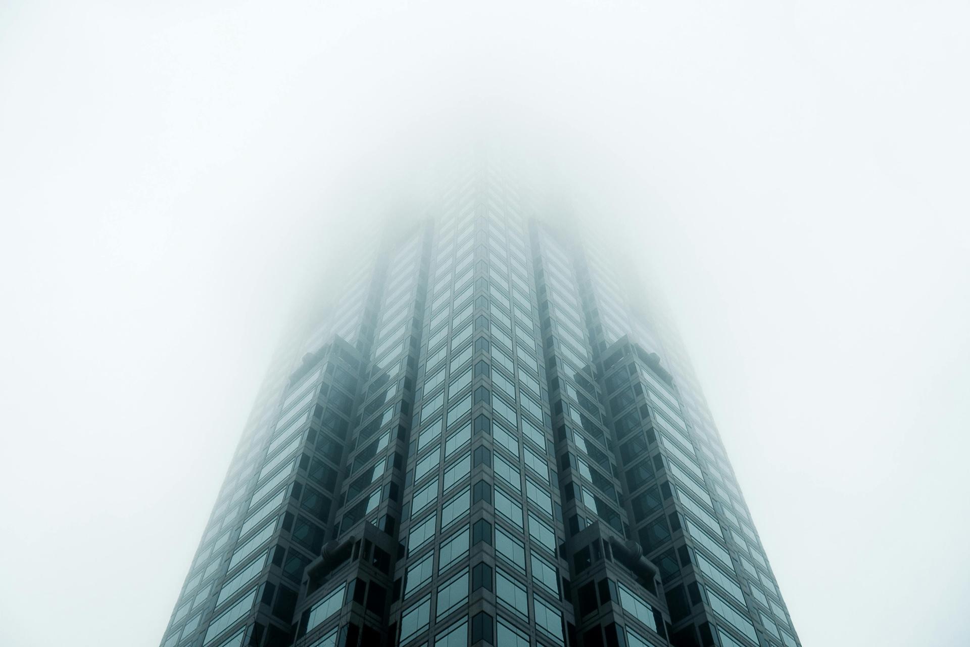 Modern skyscraper disappearing into fog, photographed from below with symmetrical glass facade architecture