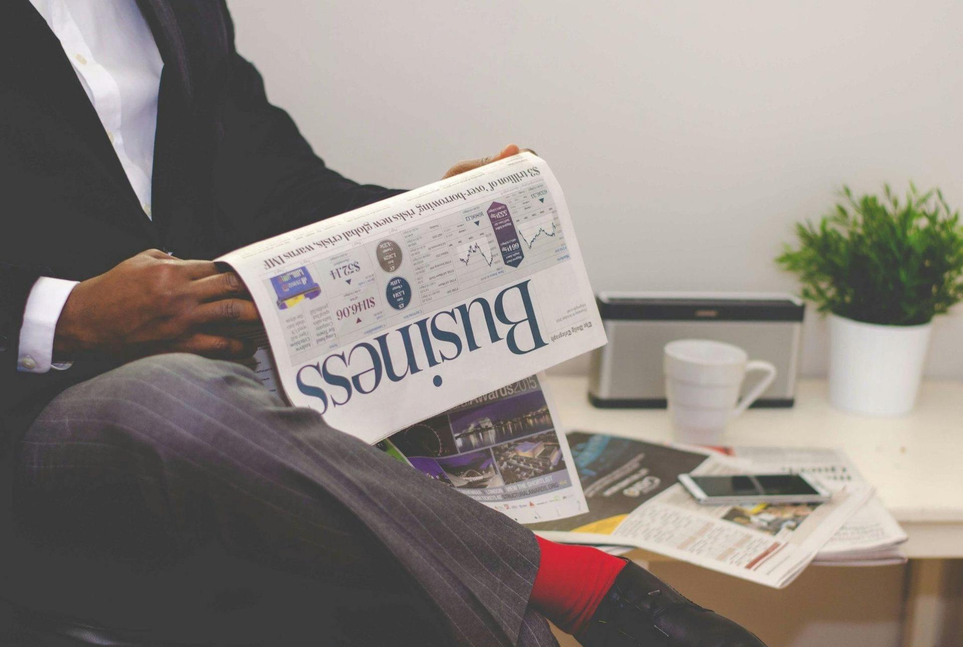 Person in business suit reading Business newspaper, with coffee cup and plant in background on desk